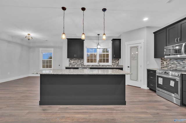 kitchen with pendant lighting, stainless steel appliances, light stone countertops, and a kitchen island