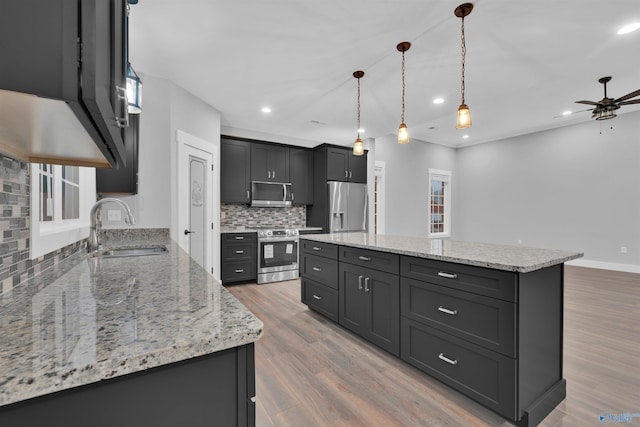 kitchen featuring pendant lighting, sink, appliances with stainless steel finishes, a center island, and light stone countertops