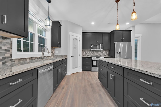 kitchen with light stone counters, appliances with stainless steel finishes, decorative light fixtures, and sink