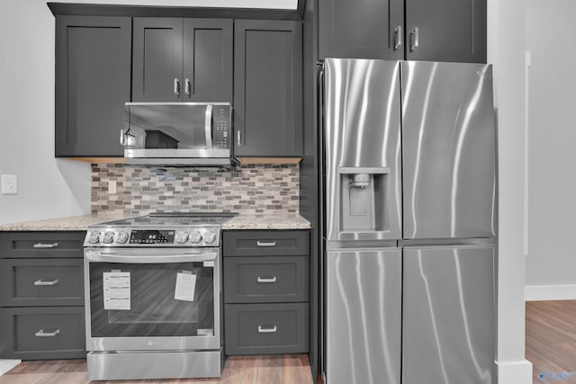 kitchen featuring light stone counters, wood-type flooring, gray cabinets, stainless steel appliances, and decorative backsplash