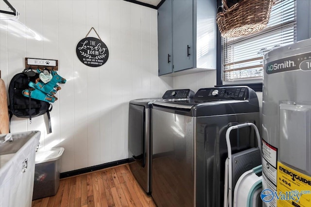 washroom with wooden walls, electric water heater, wood-type flooring, washing machine and dryer, and cabinets