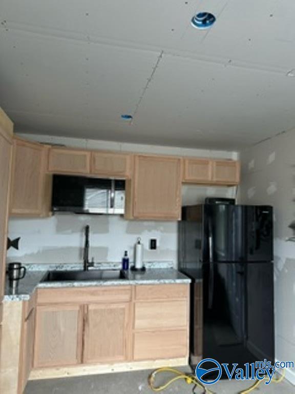 kitchen featuring black refrigerator, concrete flooring, light brown cabinetry, and sink