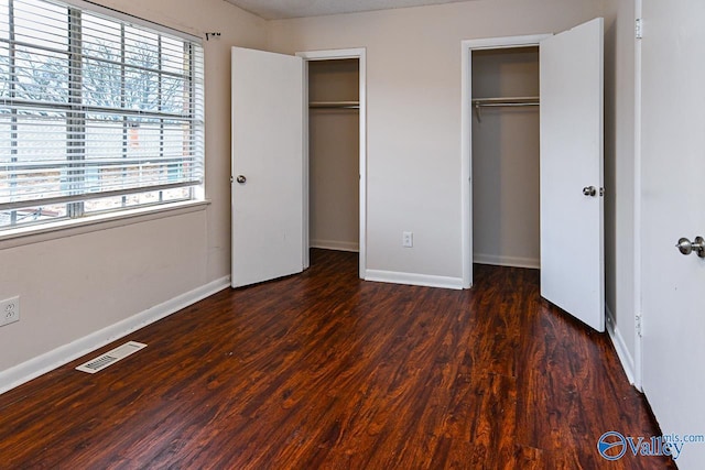 unfurnished bedroom featuring multiple closets and dark wood-type flooring