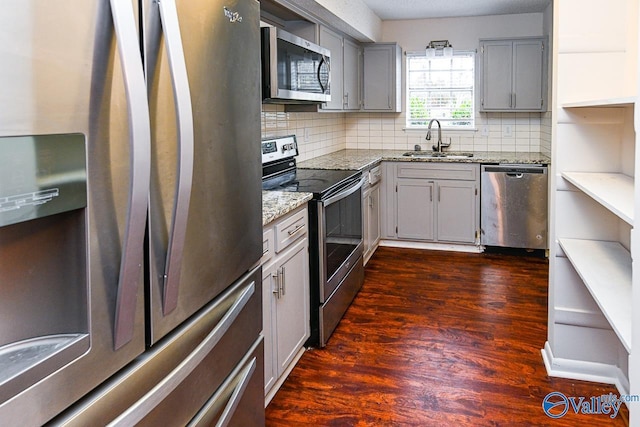 kitchen with gray cabinets, sink, light stone counters, stainless steel appliances, and dark wood-type flooring