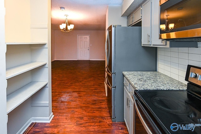 kitchen featuring hanging light fixtures, appliances with stainless steel finishes, dark hardwood / wood-style floors, a notable chandelier, and light stone countertops