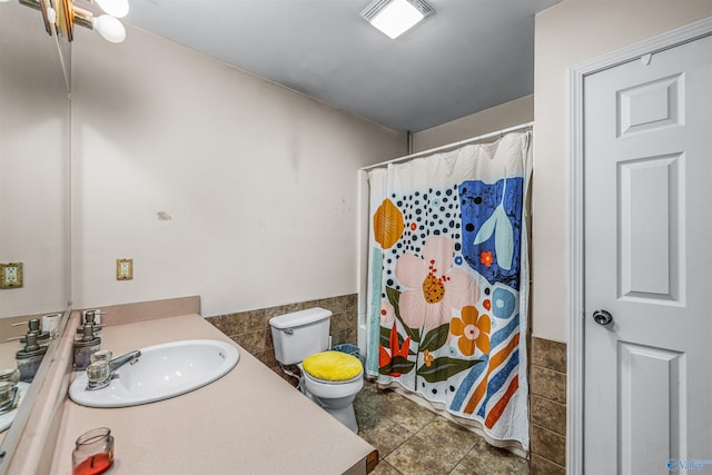 bathroom featuring tile patterned floors, vanity, toilet, and tile walls