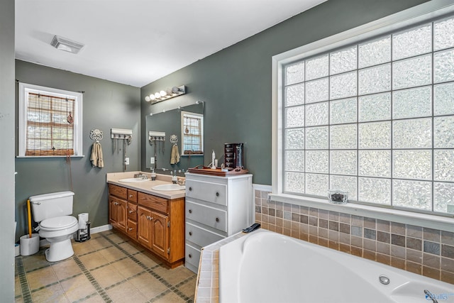 bathroom with vanity, a healthy amount of sunlight, a relaxing tiled tub, and toilet