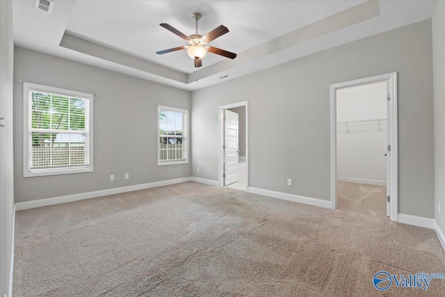 unfurnished bedroom featuring a tray ceiling, carpet floors, baseboards, a spacious closet, and ensuite bath