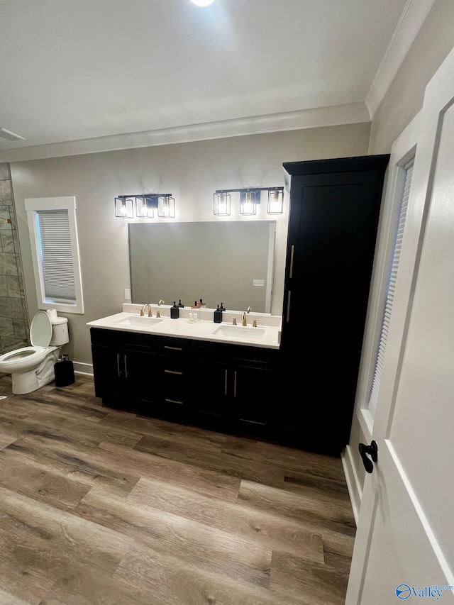 bathroom with toilet, wood-type flooring, crown molding, and double vanity