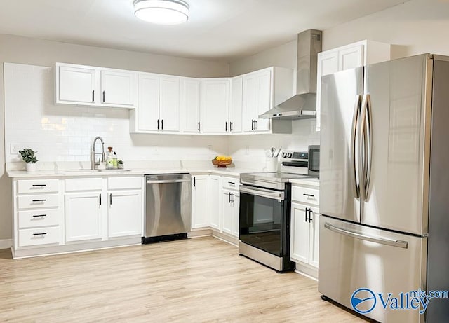 kitchen featuring stainless steel appliances, light countertops, light wood-style flooring, a sink, and wall chimney range hood