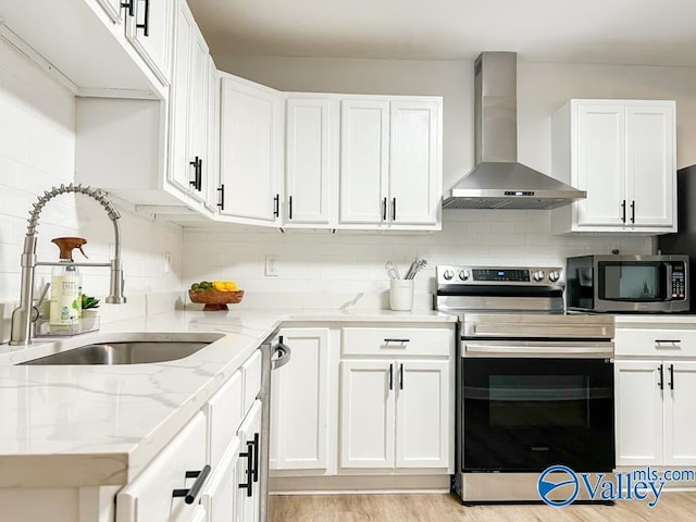 kitchen featuring backsplash, appliances with stainless steel finishes, white cabinetry, a sink, and wall chimney range hood