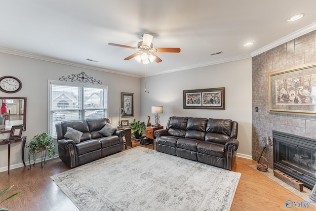 living room with a tile fireplace, hardwood / wood-style flooring, ceiling fan, and crown molding