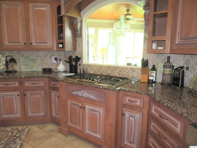 kitchen with backsplash, dark stone countertops, stainless steel gas stovetop, and light tile patterned floors