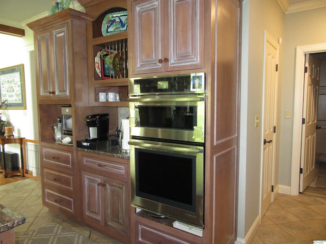 kitchen with dark stone counters, light tile patterned flooring, stainless steel double oven, and ornamental molding