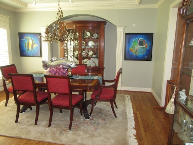 dining room featuring ornate columns, an inviting chandelier, crown molding, and hardwood / wood-style floors