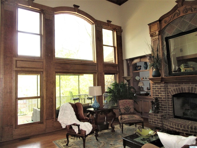 living room featuring a high ceiling, a fireplace, hardwood / wood-style flooring, and a healthy amount of sunlight