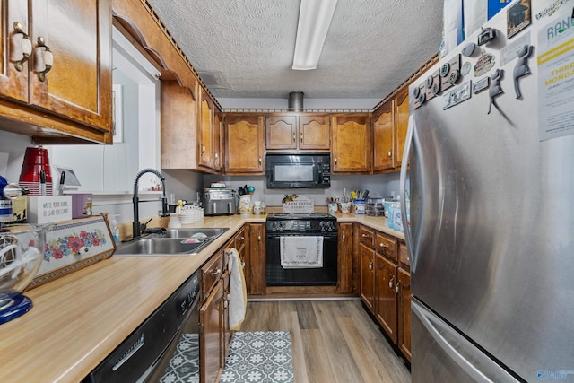 kitchen featuring sink, black appliances, a textured ceiling, and light wood-type flooring