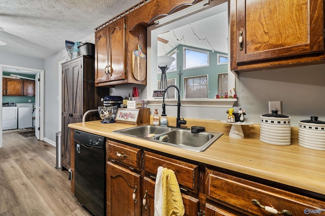 kitchen featuring sink, light hardwood / wood-style flooring, separate washer and dryer, a textured ceiling, and black dishwasher