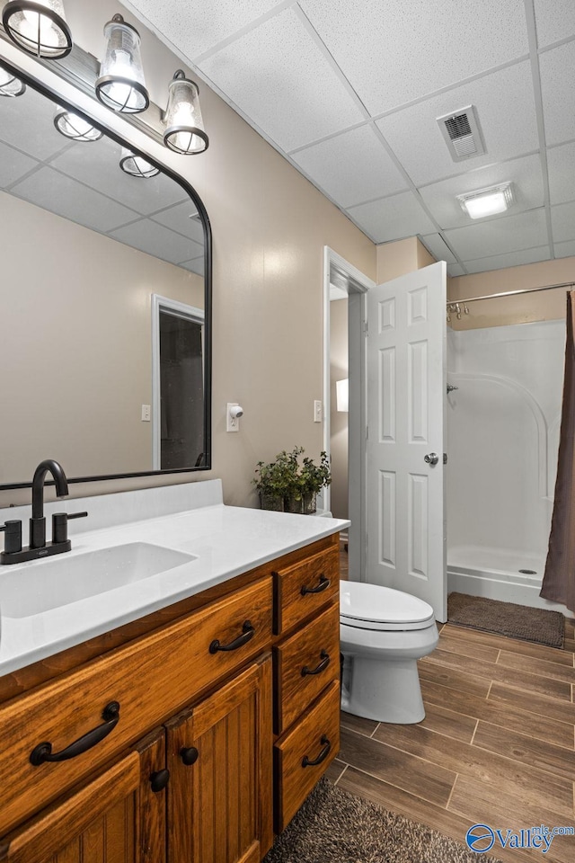 bathroom featuring a drop ceiling, vanity, hardwood / wood-style flooring, walk in shower, and toilet