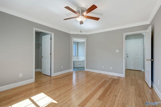 unfurnished bedroom featuring light wood-type flooring, a walk in closet, a closet, crown molding, and baseboards