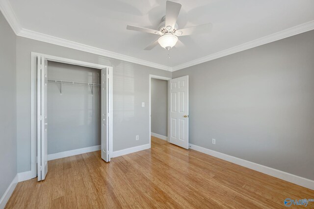 unfurnished bedroom with a ceiling fan, wood finished floors, baseboards, ornamental molding, and a closet