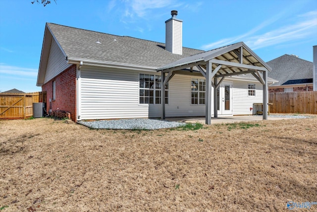 rear view of property with brick siding, fence, central air condition unit, a chimney, and a patio area