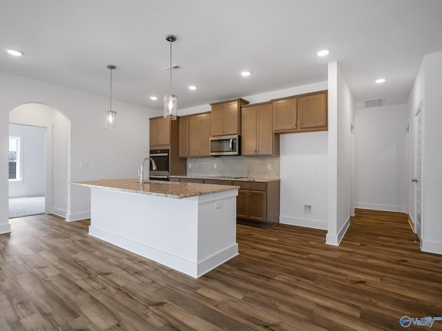 kitchen with hanging light fixtures, an island with sink, dark hardwood / wood-style flooring, and stainless steel appliances