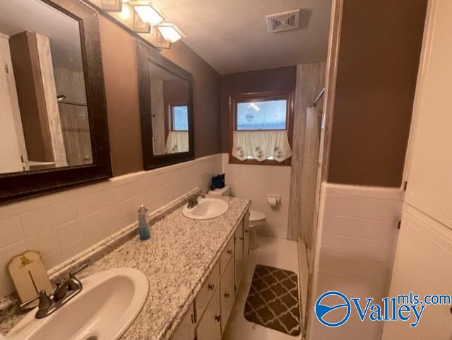 full bathroom featuring wainscoting, a sink, visible vents, and double vanity