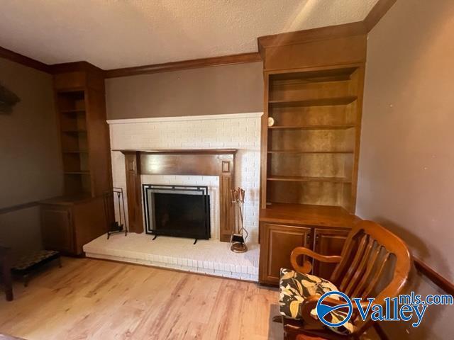 living area featuring light wood-style flooring, a fireplace, ornamental molding, and a textured ceiling