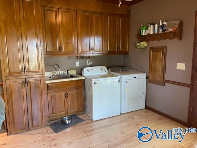 clothes washing area with cabinet space, baseboards, light wood-type flooring, separate washer and dryer, and a sink