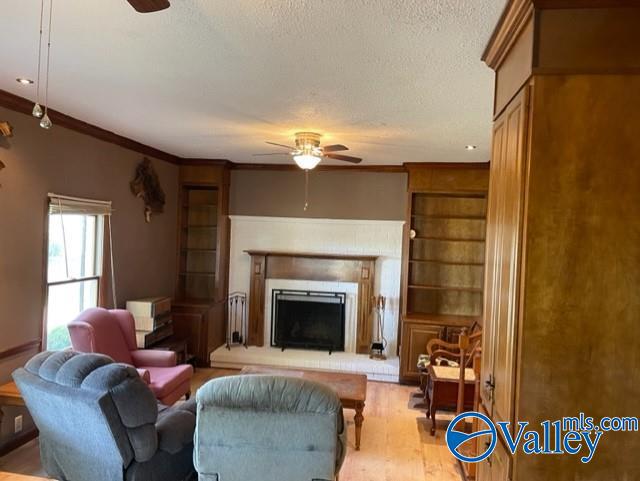 living room with a fireplace with raised hearth, ornamental molding, a ceiling fan, and light wood-style floors