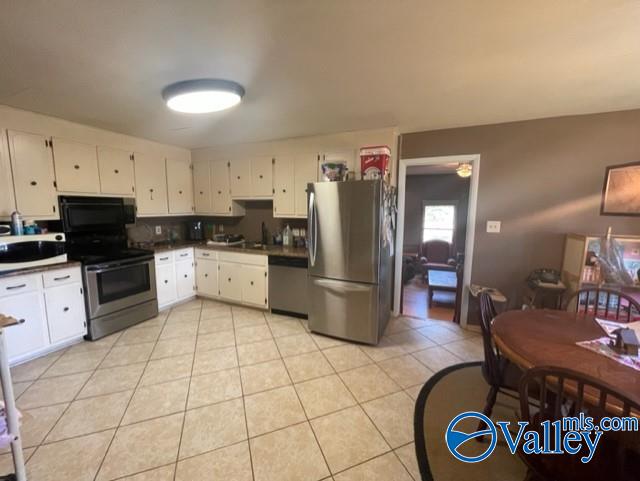 kitchen with white cabinets, light tile patterned floors, dark countertops, and stainless steel appliances