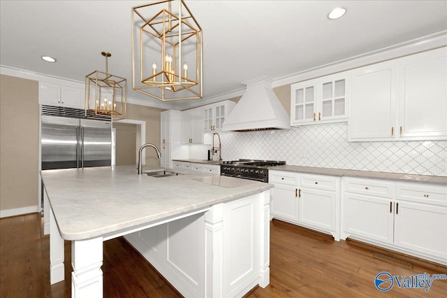 kitchen with premium range hood, a sink, an island with sink, glass insert cabinets, and pendant lighting