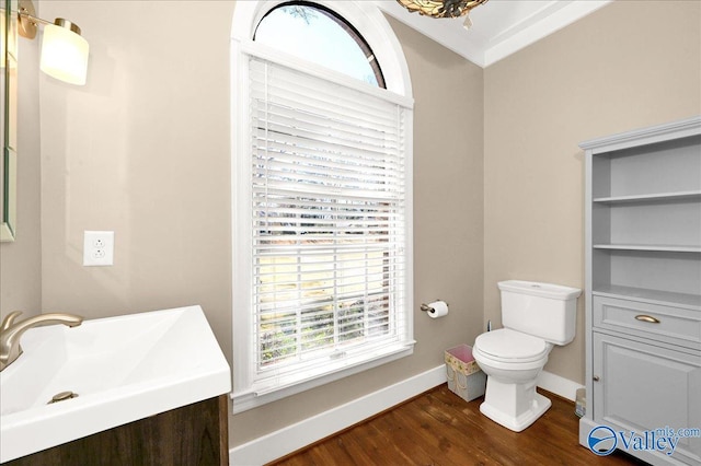 half bathroom featuring baseboards, toilet, wood finished floors, crown molding, and vanity