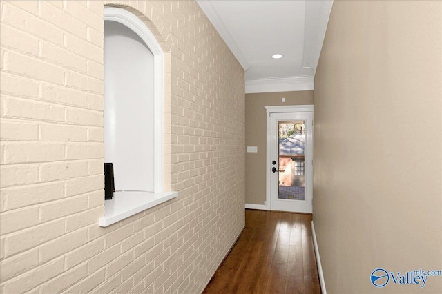 corridor featuring baseboards, brick wall, ornamental molding, and wood finished floors