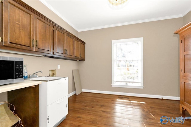 clothes washing area featuring baseboards, washer hookup, dark wood-type flooring, and ornamental molding