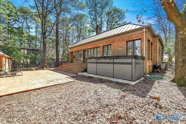 exterior space with a hot tub, metal roof, a standing seam roof, a patio area, and brick siding