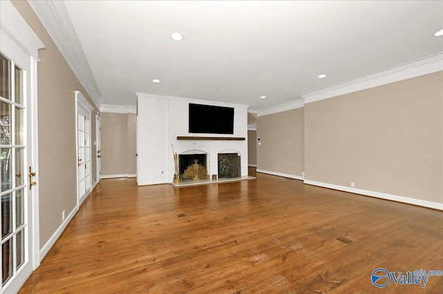 unfurnished living room with ornamental molding, a fireplace with raised hearth, baseboards, and wood finished floors