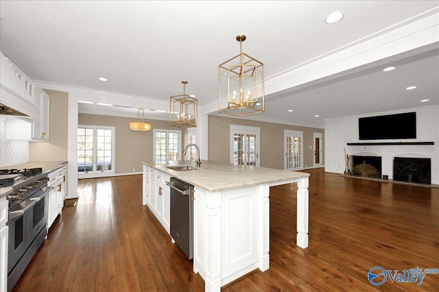 kitchen with decorative light fixtures, white cabinets, open floor plan, appliances with stainless steel finishes, and a center island with sink