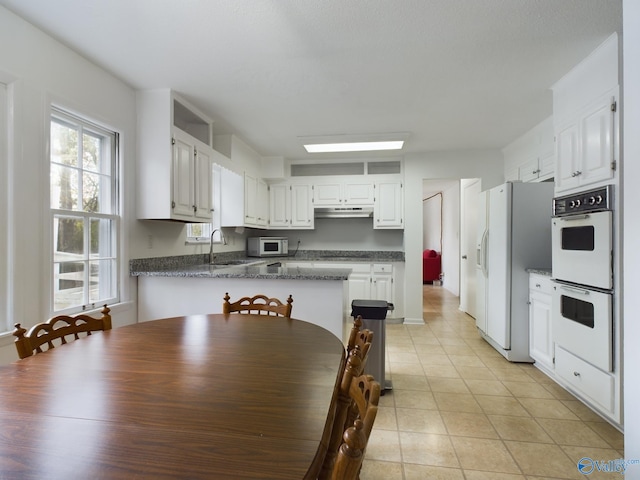 kitchen with white cabinets, kitchen peninsula, sink, light tile patterned floors, and white appliances