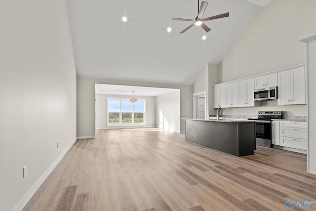 kitchen featuring an island with sink, light wood-type flooring, high vaulted ceiling, stainless steel appliances, and white cabinetry