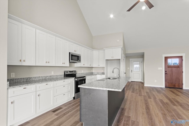 kitchen featuring high vaulted ceiling, light stone counters, white cabinets, appliances with stainless steel finishes, and a center island with sink