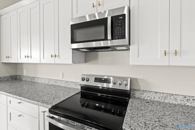 kitchen with stainless steel appliances, light stone countertops, and white cabinets