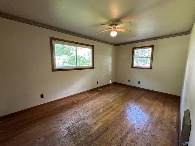 empty room with crown molding, wood-type flooring, visible vents, a ceiling fan, and baseboards