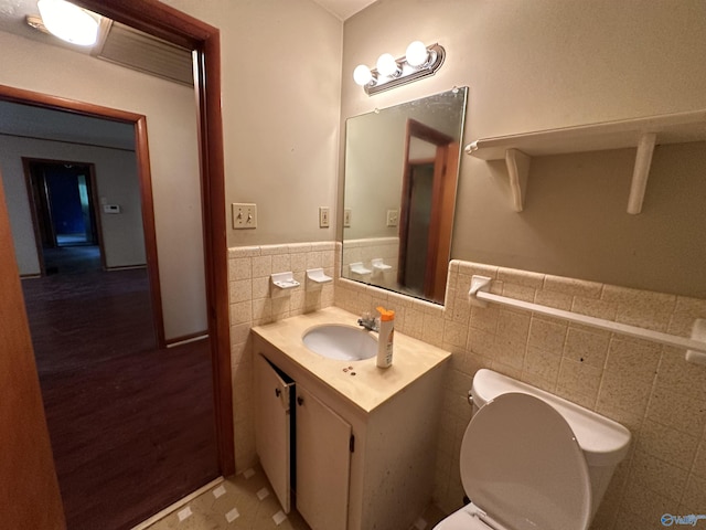 half bathroom featuring wainscoting, tile walls, toilet, and vanity