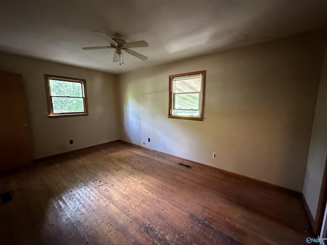 empty room featuring hardwood / wood-style flooring, ceiling fan, visible vents, and baseboards