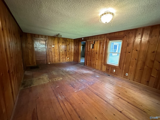 empty room featuring wooden walls, hardwood / wood-style floors, and a textured ceiling