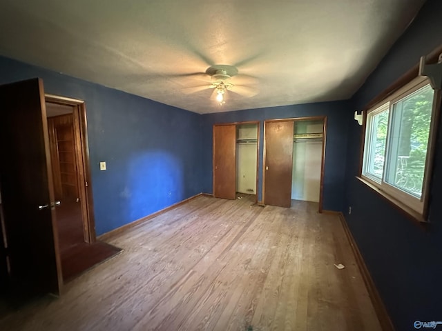 unfurnished bedroom with baseboards, wood finished floors, a ceiling fan, and multiple closets