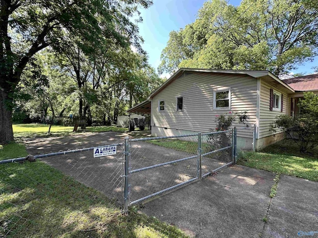 view of side of home with crawl space, a lawn, fence, and a gate