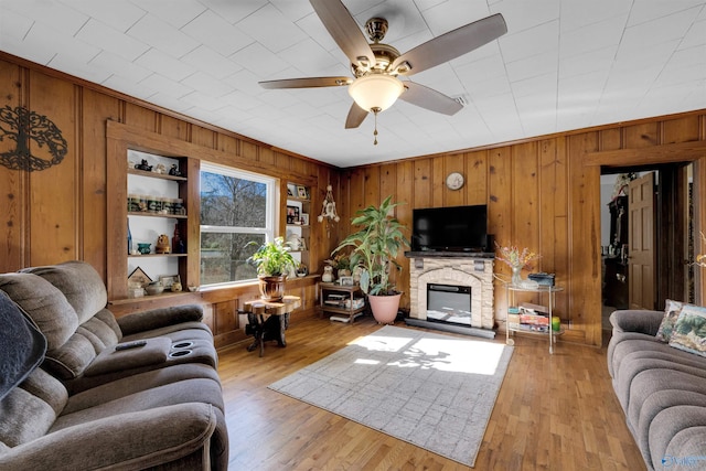 living room featuring ceiling fan, light hardwood / wood-style flooring, wood walls, and a stone fireplace